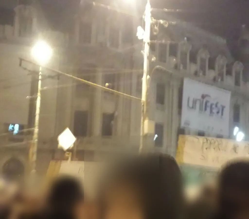 Clădirea Universității luminată noaptea, cu pancarte ridicate deasupra mulțimii